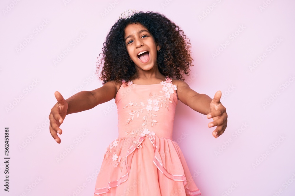 African american child with curly hair wearing princess crown looking at the camera smiling with open arms for hug. cheerful expression embracing happiness. African american child with curly hair wearing princess crown looking at the camera smiling with open arms for hug. cheerful expression embracing happiness.
