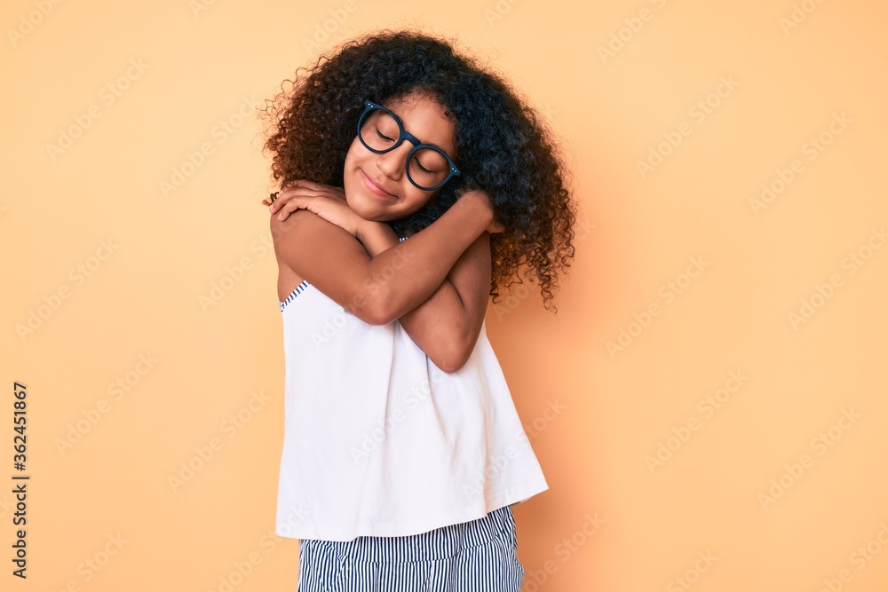 African american child with curly hair wearing casual clothes and glasses hugging oneself happy and positive, smiling confident. self love and self care African american child with curly hair wearing casual clothes and glasses hugging oneself happy and positive, smiling confident. self love and self care