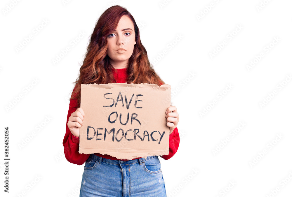 Young beautiful woman holding save our democracy protest banner thinking attitude and sober expression looking self confident Young beautiful woman holding save our democracy protest banner thinking attitude and sober expression looking self confident