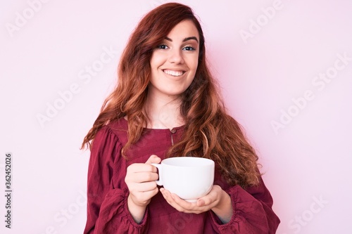 Young beautiful woman holding coffee looking positive and happy standing and smiling with a confident smile showing teeth