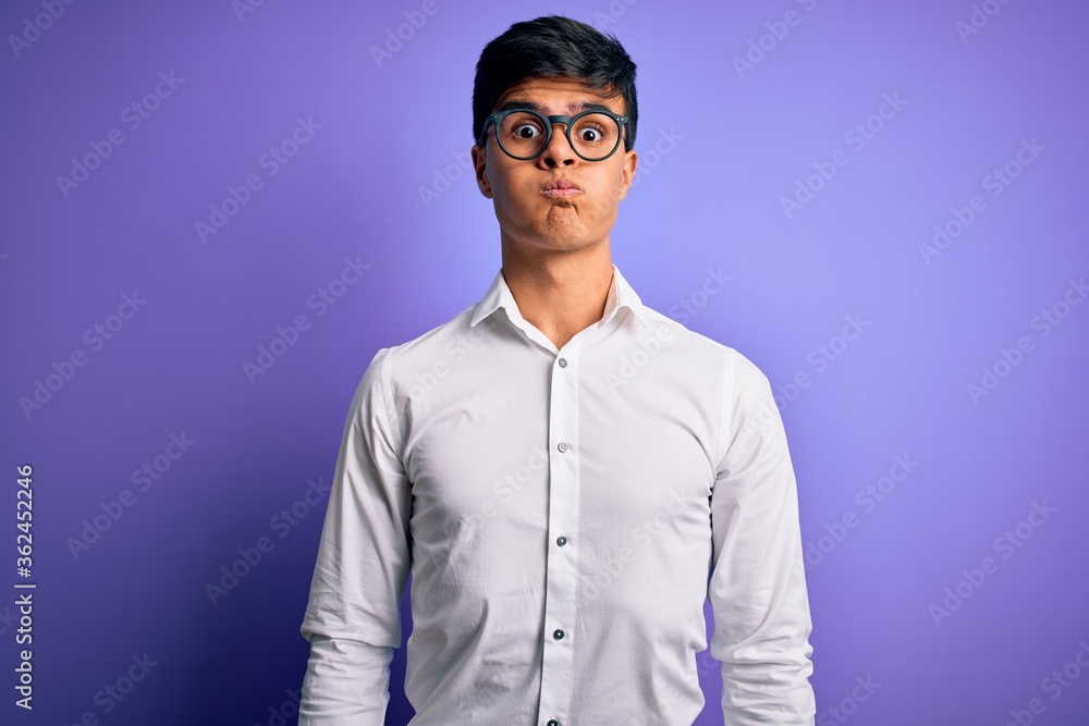Young handsome business man wearing shirt and glasses over isolated purple background puffing cheeks with funny face. Mouth inflated with air, crazy expression. Young handsome business man wearing shirt and glasses over isolated purple background puffing cheeks with funny face. Mouth inflated with air, crazy expression.