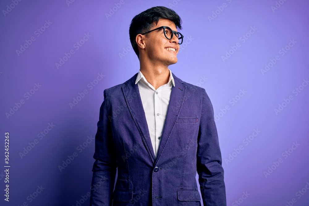Young handsome business man wearing jacket and glasses over isolated purple background looking away to side with smile on face, natural expression. Laughing confident. Young handsome business man wearing jacket and glasses over isolated purple background looking away to side with smile on face, natural expression. Laughing confident.