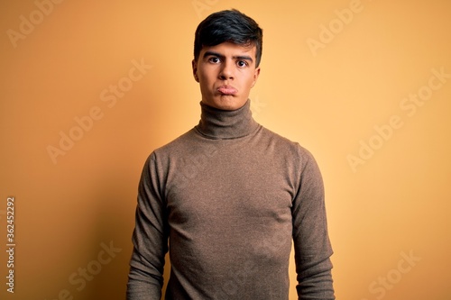 Young handsome man wearing casual turtleneck sweater over isolated yellow background depressed and worry for distress, crying angry and afraid. Sad expression.