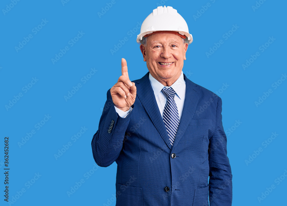 Senior handsome grey-haired man wearing suit and architect hardhat showing and pointing up with finger number one while smiling confident and happy. Senior handsome grey-haired man wearing suit and architect hardhat showing and pointing up with finger number one while smiling confident and happy.
