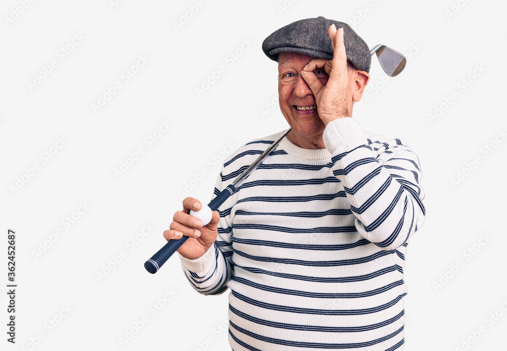 Senior handsome grey-haired man holding golf club and ball smiling happy doing ok sign with hand on eye looking through fingers Senior handsome grey-haired man holding golf club and ball smiling happy doing ok sign with hand on eye looking through fingers