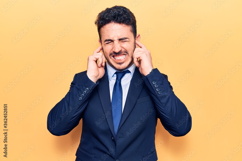 Young hispanic man wearing suit covering ears with fingers with annoyed expression for the noise of loud music. deaf concept. Young hispanic man wearing suit covering ears with fingers with annoyed expression for the noise of loud music. deaf concept.