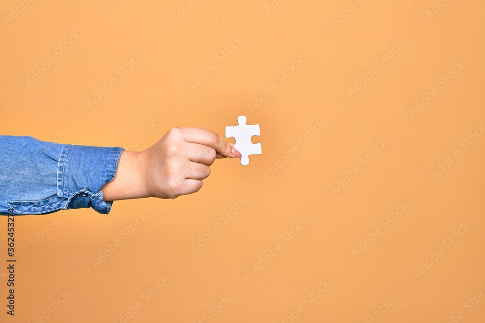 Hand of caucasian young woman holding piece of puzzle over isolated yellow background Hand of caucasian young woman holding piece of puzzle over isolated yellow background