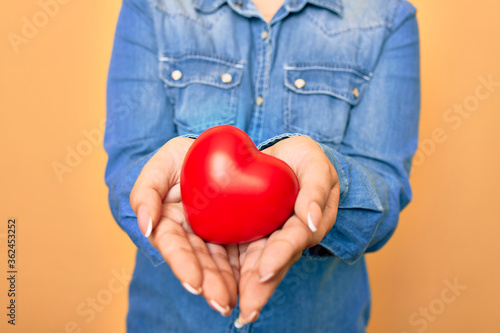 Fototapeta Naklejka Na Ścianę i Meble -  Woman holding red heart with two hands standing over isolated yellow background