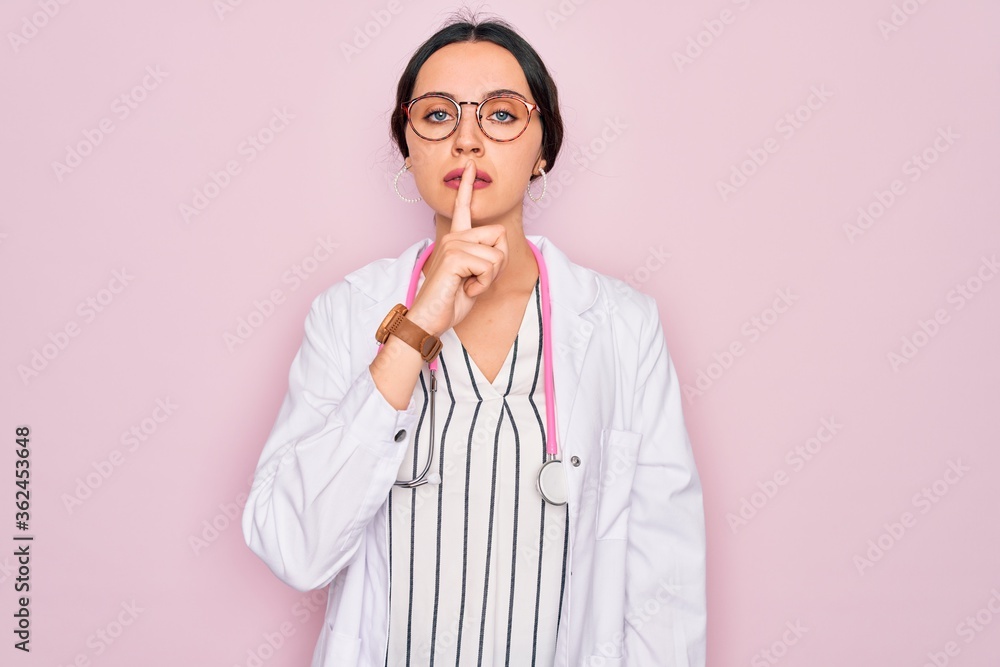 Beautiful doctor woman with blue eyes wearing coat and stethoscope over pink background asking to be quiet with finger on lips. Silence and secret concept. Beautiful doctor woman with blue eyes wearing coat and stethoscope over pink background asking to be quiet with finger on lips. Silence and secret concept.