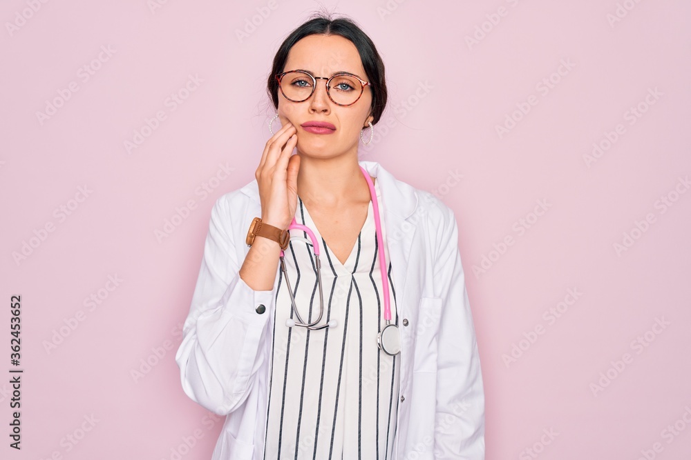 Beautiful doctor woman with blue eyes wearing coat and stethoscope over pink background touching mouth with hand with painful expression because of toothache or dental illness on teeth. Dentist Beautiful doctor woman with blue eyes wearing coat and stethoscope over pink background touching mouth with hand with painful expression because of toothache or dental illness on teeth. Dentist