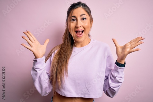 Young beautiful sport woman wearing sweatshirt over pink isolated background celebrating crazy and amazed for success with arms raised and open eyes screaming excited. Winner concept