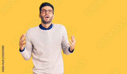Young handsome hispanic man wearing elegant clothes and glasses crazy and mad shouting and yelling with aggressive expression and arms raised. frustration concept.