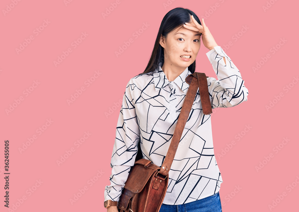 Fototapeta premium Young beautiful chinese woman holding briefcase stressed and frustrated with hand on head, surprised and angry face