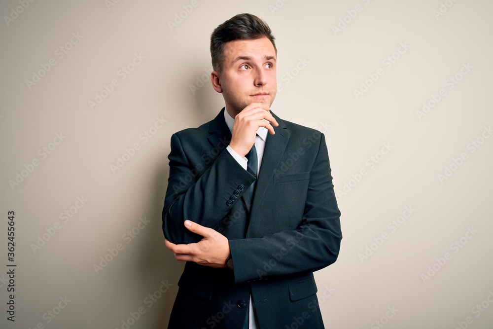 Young handsome business man wearing elegant suit and tie over isolated background with hand on chin thinking about question, pensive expression. Smiling with thoughtful face. Doubt concept. Young handsome business man wearing elegant suit and tie over isolated background with hand on chin thinking about question, pensive expression. Smiling with thoughtful face. Doubt concept.