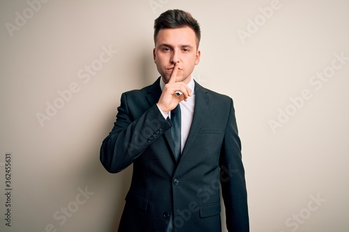 Young handsome business man wearing elegant suit and tie over isolated background asking to be quiet with finger on lips. Silence and secret concept.