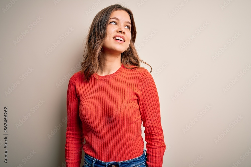 Young blonde girl wearing casual red sweater over isolated background looking away to side with smile on face, natural expression. Laughing confident. Young blonde girl wearing casual red sweater over isolated background looking away to side with smile on face, natural expression. Laughing confident.