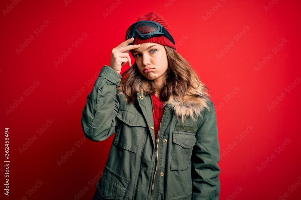 Young blonde girl wearing ski glasses and winter coat for ski weather over red background worried and stressed about a problem with hand on forehead, nervous and anxious for crisis Young blonde girl wearing ski glasses and winter coat for ski weather over red background worried and stressed about a problem with hand on forehead, nervous and anxious for crisis