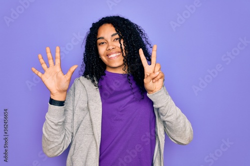 Young african american sporty woman wearing casual sweatshirt over purple background showing and pointing up with fingers number seven while smiling confident and happy. © Krakenimages.com