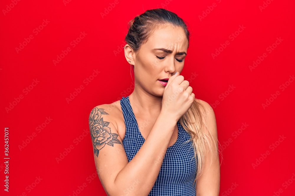 Young beautiful blonde woman wearing sporty t-shirt standing over isolated red background feeling unwell and coughing as symptom for cold or bronchitis. Health care concept. Young beautiful blonde woman wearing sporty t-shirt standing over isolated red background feeling unwell and coughing as symptom for cold or bronchitis. Health care concept.