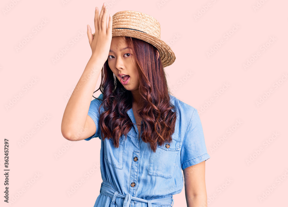 Young beautiful chinese girl wearing summer hat surprised with hand on head for mistake, remember error. forgot, bad memory concept. Young beautiful chinese girl wearing summer hat surprised with hand on head for mistake, remember error. forgot, bad memory concept.