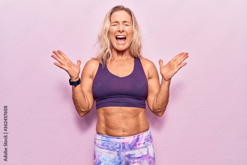 Middle age caucasian blonde woman wearing sportswear over pink background celebrating mad and crazy for success with arms raised and closed eyes screaming excited. winner concept Middle age caucasian blonde woman wearing sportswear over pink background celebrating mad and crazy for success with arms raised and closed eyes screaming excited. winner concept