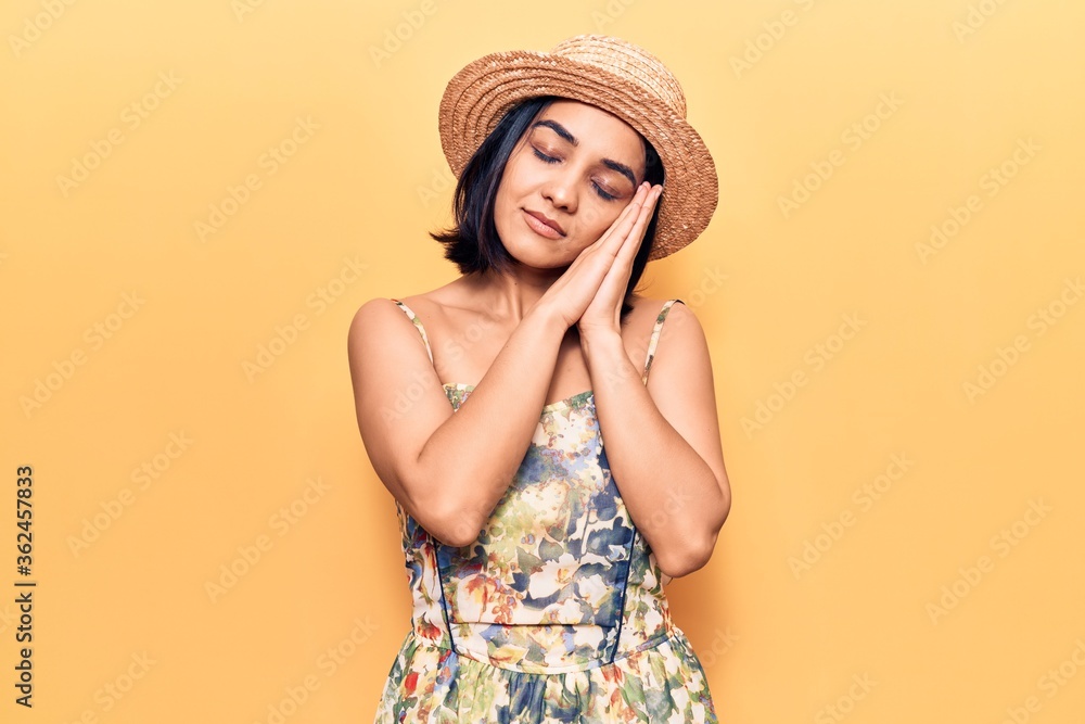 Young beautiful latin woman wearing summer hat sleeping tired dreaming and posing with hands together while smiling with closed eyes. Young beautiful latin woman wearing summer hat sleeping tired dreaming and posing with hands together while smiling with closed eyes.