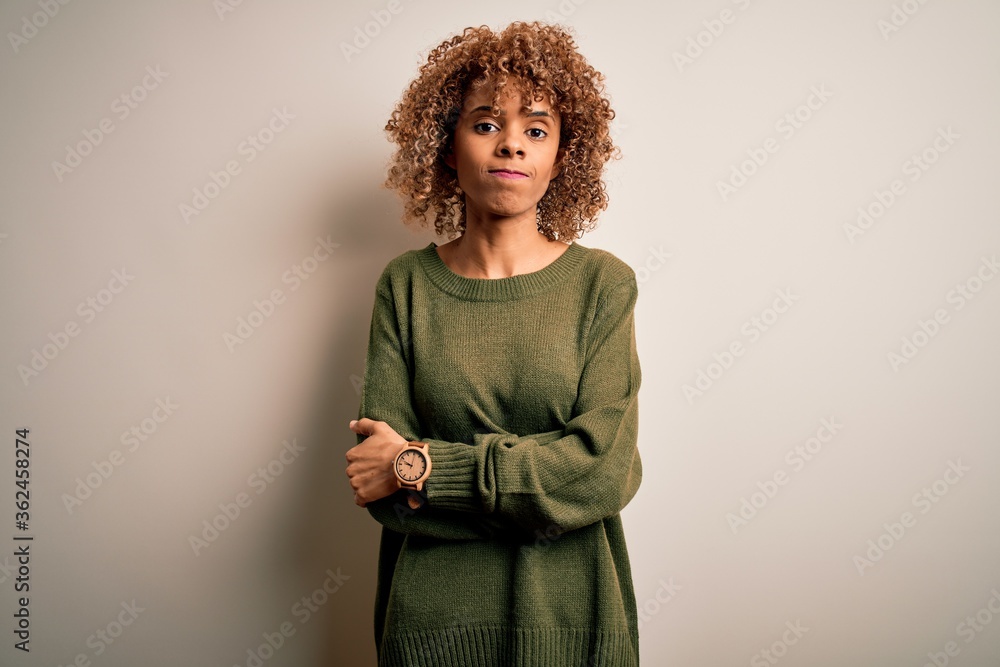 Beautiful african american woman with curly hair wearing casual sweater over white background skeptic and nervous, disapproving expression on face with crossed arms. Negative person. Beautiful african american woman with curly hair wearing casual sweater over white background skeptic and nervous, disapproving expression on face with crossed arms. Negative person.