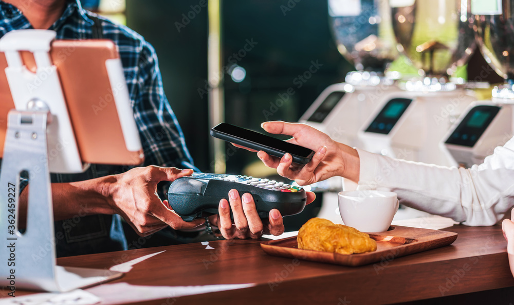 Closeup Asian customer man hand paying money via contactless channel by mobile banking application to Small business owner at table in cafe shop, Small business owner and startup in coffee shop. Closeup Asian customer man hand paying money via contactless channel by mobile banking application to Small business owner at table in cafe shop, Small business owner and startup in coffee shop.