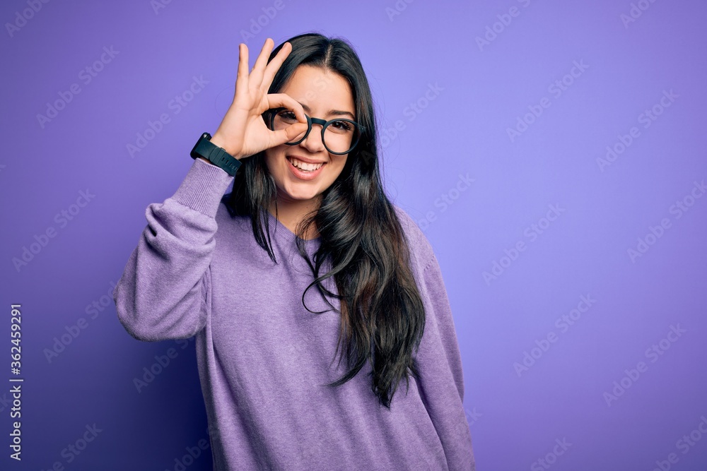Young brunette woman wearing glasses over purple isolated background doing ok gesture with hand smiling, eye looking through fingers with happy face. Young brunette woman wearing glasses over purple isolated background doing ok gesture with hand smiling, eye looking through fingers with happy face.