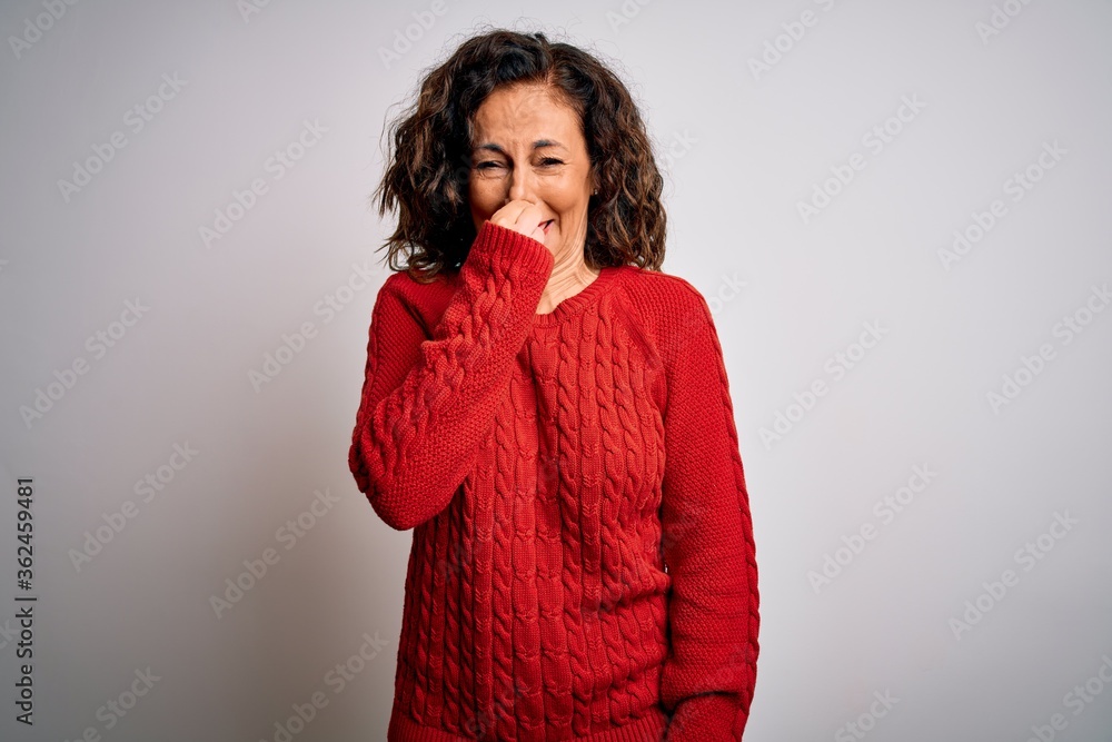 Middle age brunette woman wearing casual sweater standing over isolated white background smelling something stinky and disgusting, intolerable smell, holding breath with fingers on nose. Bad smell Middle age brunette woman wearing casual sweater standing over isolated white background smelling something stinky and disgusting, intolerable smell, holding breath with fingers on nose. Bad smell