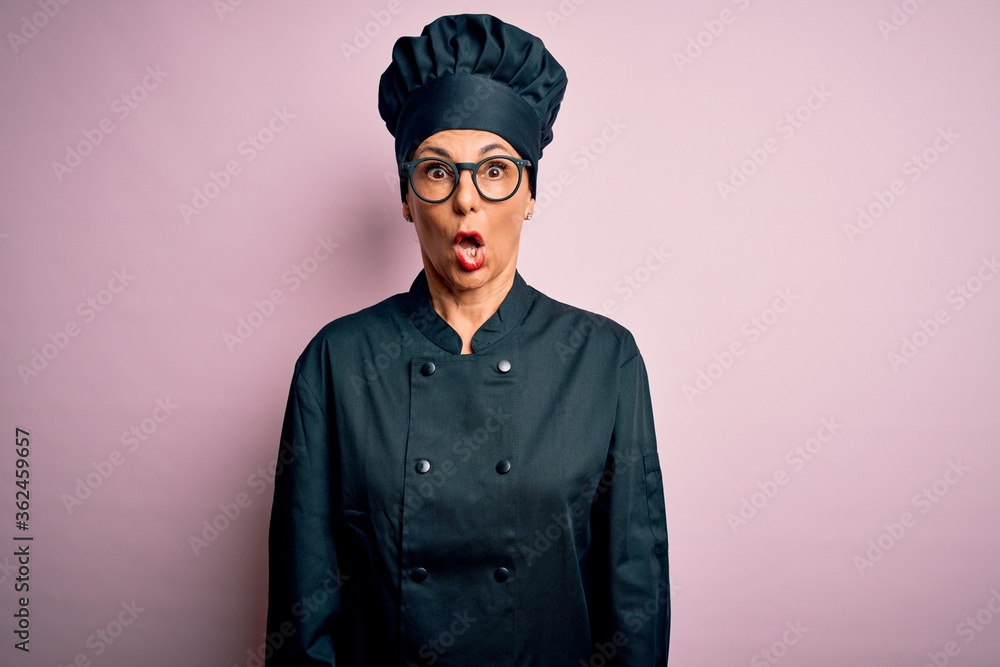 Middle age brunette chef woman wearing cooker uniform and hat over isolated pink background afraid and shocked with surprise and amazed expression, fear and excited face. Middle age brunette chef woman wearing cooker uniform and hat over isolated pink background afraid and shocked with surprise and amazed expression, fear and excited face.