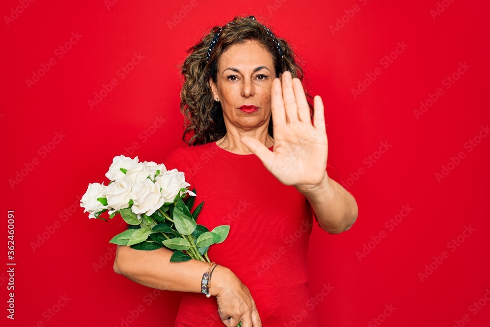 Middle age senior woman holding romantic bouquet of white roses over red background with open hand doing stop sign with serious and confident expression, defense gesture Middle age senior woman holding romantic bouquet of white roses over red background with open hand doing stop sign with serious and confident expression, defense gesture
