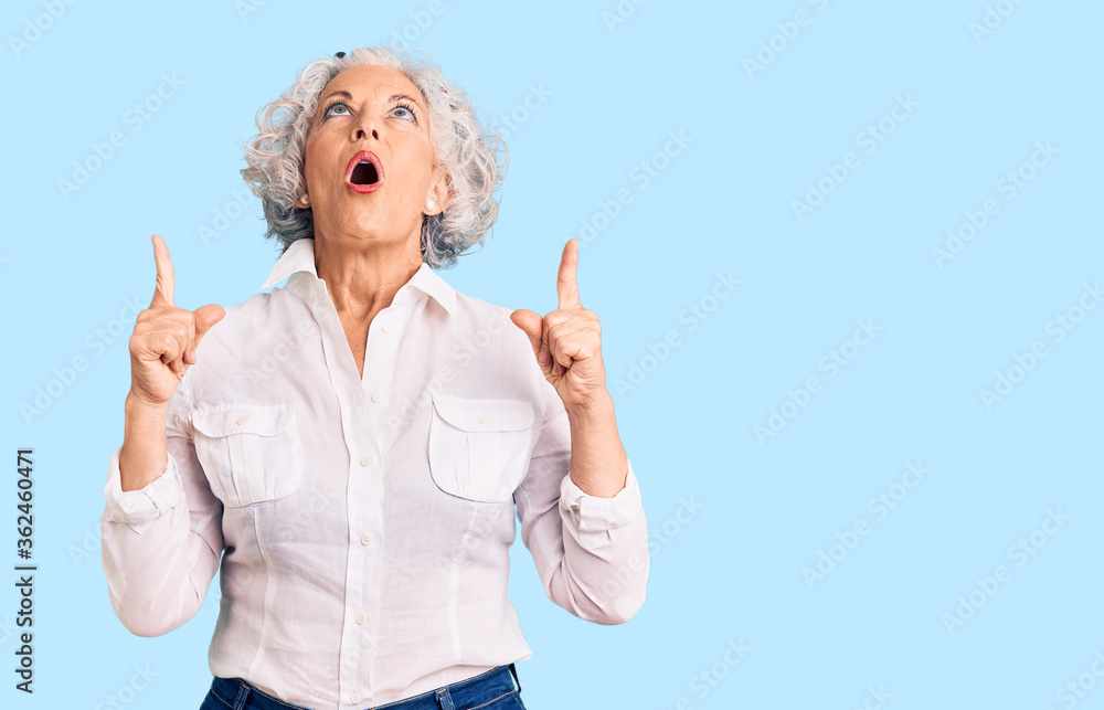 Senior grey-haired woman wearing casual clothes amazed and surprised looking up and pointing with fingers and raised arms. Senior grey-haired woman wearing casual clothes amazed and surprised looking up and pointing with fingers and raised arms.