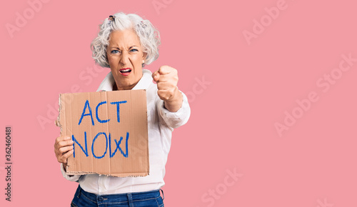 Foto Senior grey-haired woman holding act now banner annoyed and frustrated shouting