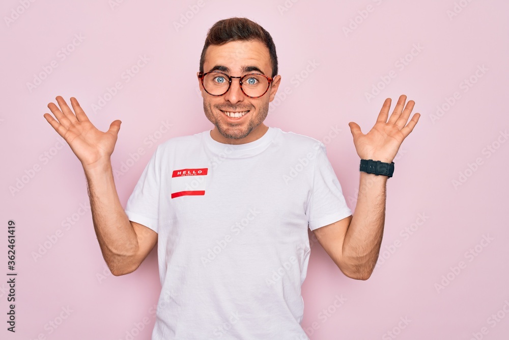 Fototapeta premium Handsome man with blue eyes wearing sticker with hello my name is message identification celebrating crazy and amazed for success with arms raised and open eyes screaming excited. Winner concept