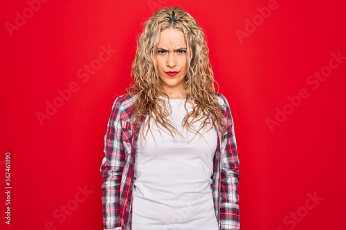 Young beautiful blonde woman wearing casual shirt standing over isolated red background skeptic and nervous, frowning upset because of problem. Negative person.