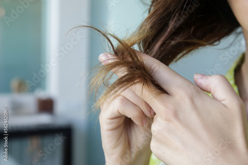 Woman looking at her dry and tangled hair ends.