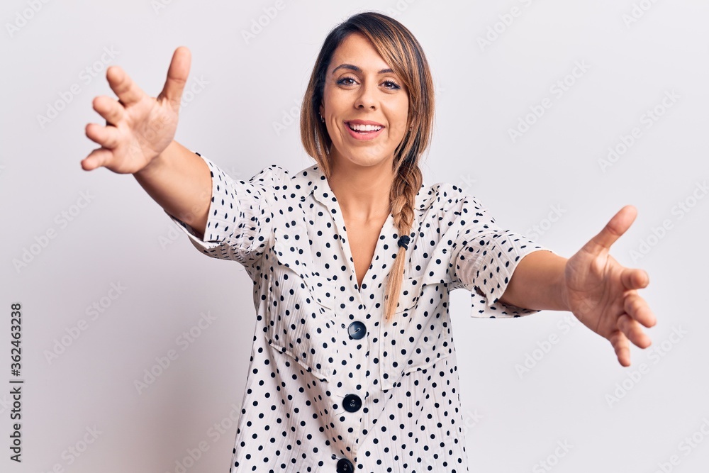 Young beautiful woman wearing casual dress looking at the camera smiling with open arms for hug. cheerful expression embracing happiness. Young beautiful woman wearing casual dress looking at the camera smiling with open arms for hug. cheerful expression embracing happiness.