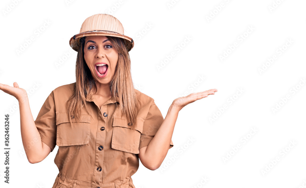Fototapeta premium Young beautiful woman wearing explorer hat celebrating victory with happy smile and winner expression with raised hands