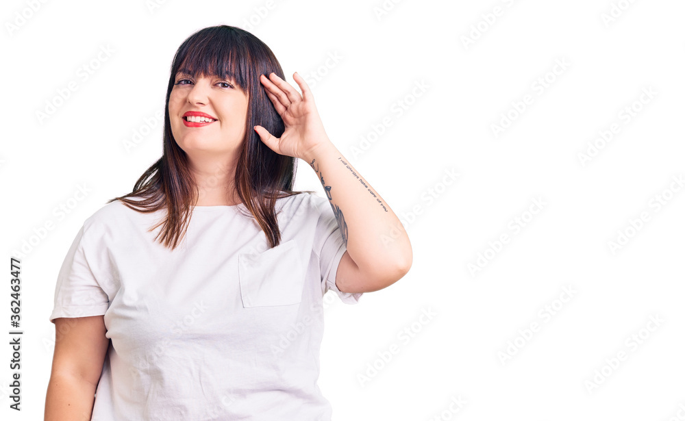 Young plus size woman wearing casual clothes smiling with hand over ear listening an hearing to rumor or gossip. deafness concept. Young plus size woman wearing casual clothes smiling with hand over ear listening an hearing to rumor or gossip. deafness concept.