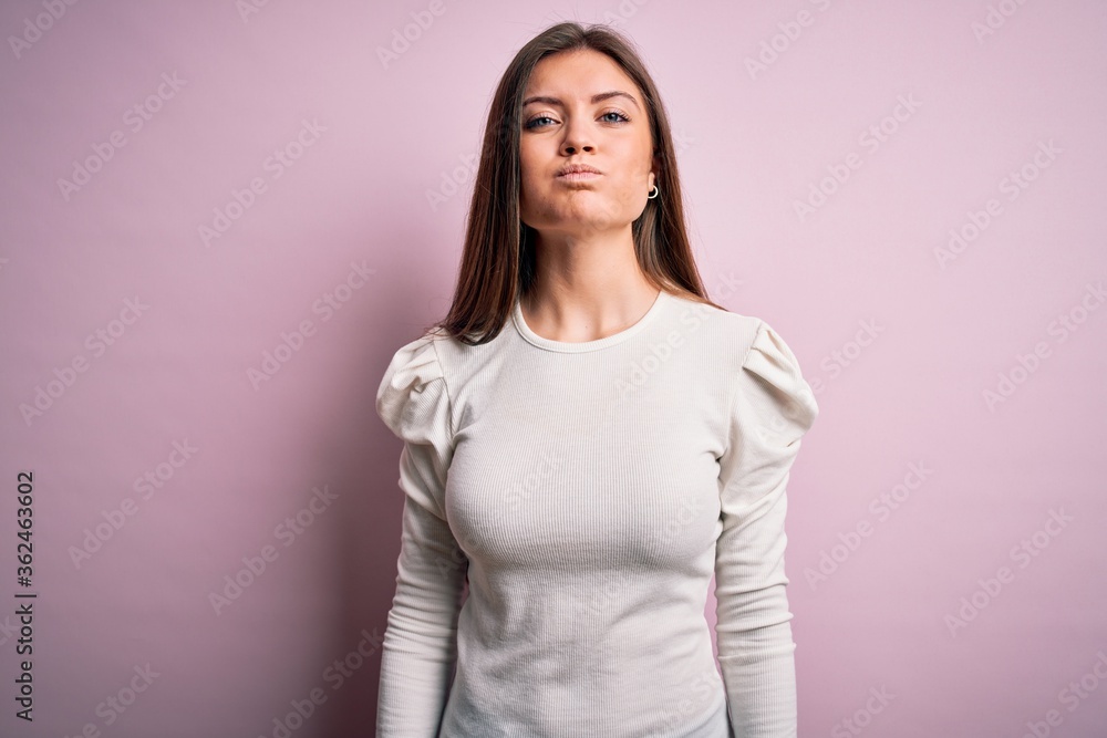 Young beautiful woman with blue eyes wearing casual white t-shirt over pink background puffing cheeks with funny face. Mouth inflated with air, crazy expression. Young beautiful woman with blue eyes wearing casual white t-shirt over pink background puffing cheeks with funny face. Mouth inflated with air, crazy expression.