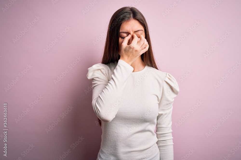 Young beautiful woman with blue eyes wearing casual white t-shirt over pink background tired rubbing nose and eyes feeling fatigue and headache. Stress and frustration concept. Young beautiful woman with blue eyes wearing casual white t-shirt over pink background tired rubbing nose and eyes feeling fatigue and headache. Stress and frustration concept.