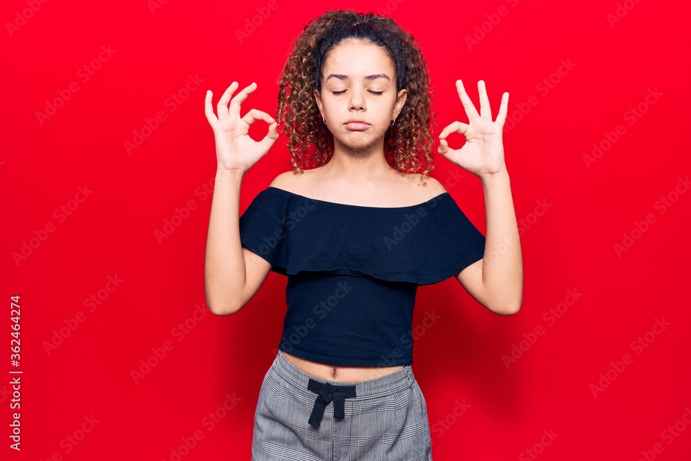 Beautiful kid girl with curly hair wearing casual clothes relax and smiling with eyes closed doing meditation gesture with fingers. yoga concept. Beautiful kid girl with curly hair wearing casual clothes relax and smiling with eyes closed doing meditation gesture with fingers. yoga concept.