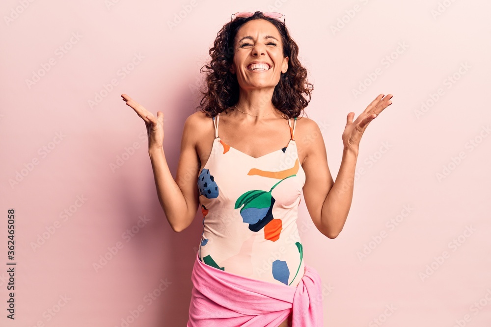 Middle age beautiful woman wearing swimwear and sunglasses celebrating mad and crazy for success with arms raised and closed eyes screaming excited. winner concept Middle age beautiful woman wearing swimwear and sunglasses celebrating mad and crazy for success with arms raised and closed eyes screaming excited. winner concept