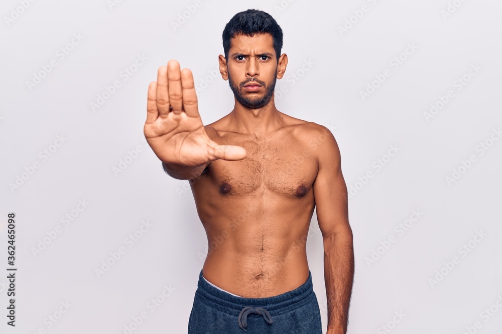 Young latin man standing shirtless doing stop sing with palm of the hand. warning expression with negative and serious gesture on the face. Young latin man standing shirtless doing stop sing with palm of the hand. warning expression with negative and serious gesture on the face.