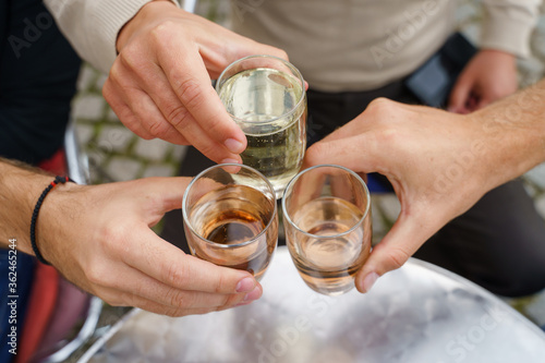 Close up on hands of unknown people holding glasses toasting - Caucasian men celebrating with wine and soda alcohol drink spricer popular in balkan countries - close up top view in day outdoor