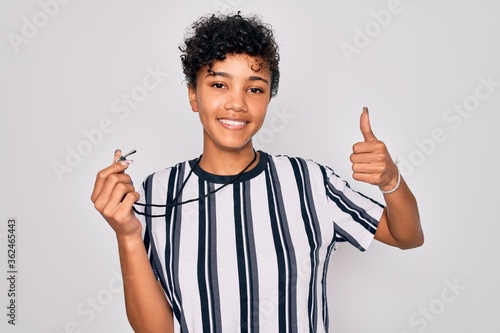 Young beautiful african american afro referee woman wearing striped uniform using whistle happy with big smile doing ok sign, thumb up with fingers, excellent sign photo