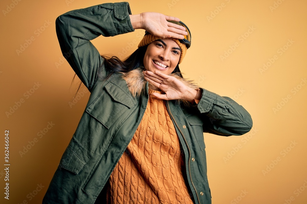 Young beautiful hispanic woman wearing ski glasses and coat for winter weather Smiling cheerful playing peek a boo with hands showing face. Surprised and exited Young beautiful hispanic woman wearing ski glasses and coat for winter weather Smiling cheerful playing peek a boo with hands showing face. Surprised and exited