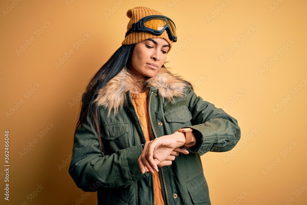 Young beautiful hispanic woman wearing ski glasses and coat for winter weather Checking the time on wrist watch, relaxed and confident Young beautiful hispanic woman wearing ski glasses and coat for winter weather Checking the time on wrist watch, relaxed and confident