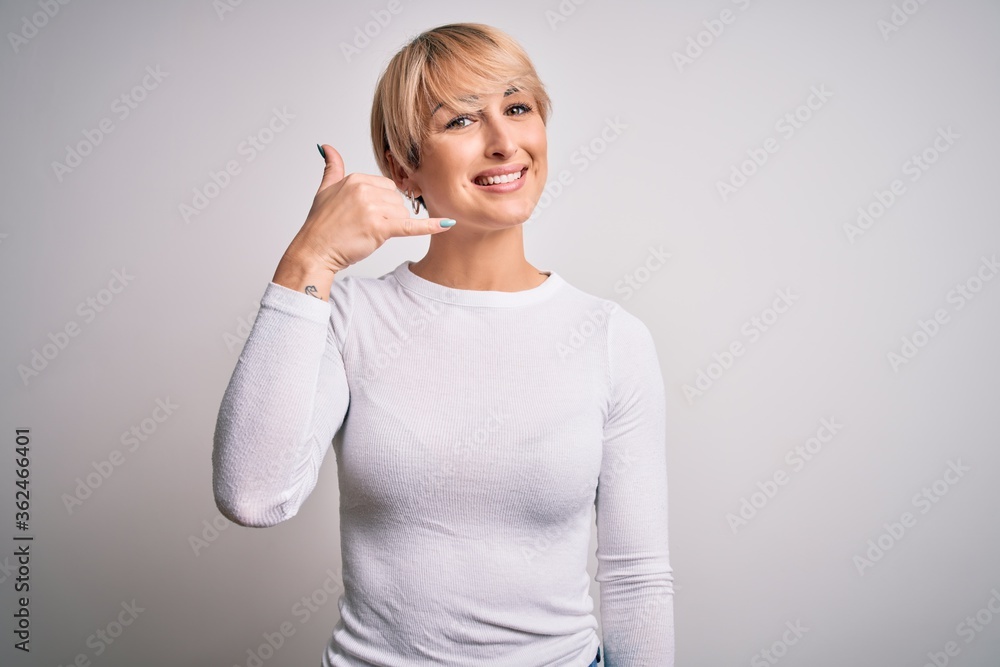 Young beautiful blonde woman with modern short hair hairstyle standing over isolated background smiling doing phone gesture with hand and fingers like talking on the telephone. Communicating concepts. Young beautiful blonde woman with modern short hair hairstyle standing over isolated background smiling doing phone gesture with hand and fingers like talking on the telephone. Communicating concepts.